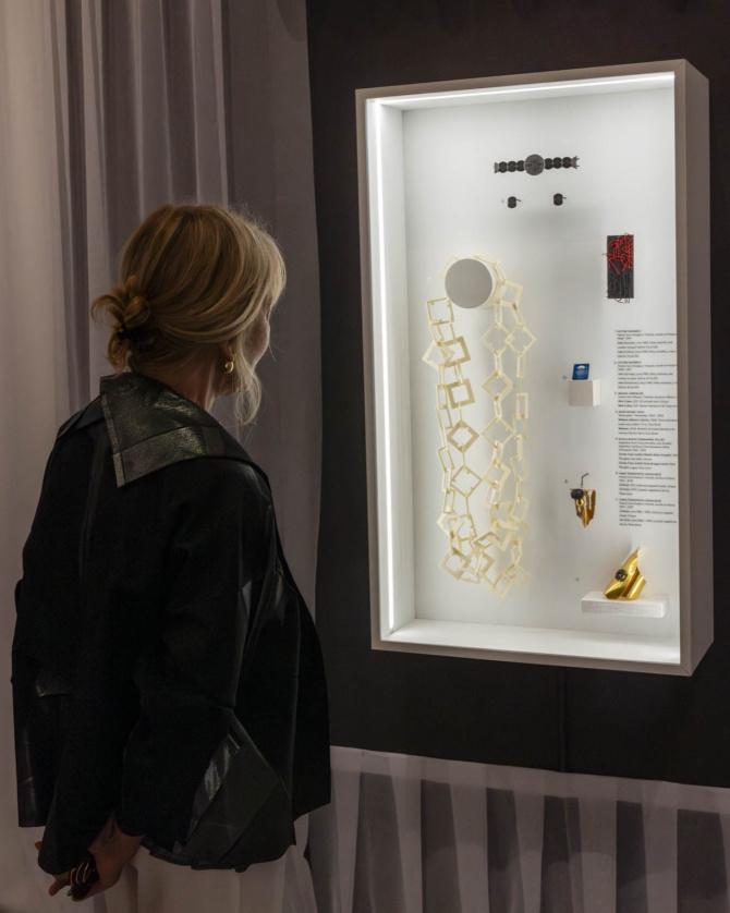 Woman Touring Artists' Jewelry Exhibit, Looking into glass display case.